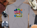 Garment Graphics’ gray hoodie features Loud & Proud in colorful text at its center, with a microphone, star, thumbs-up, and megaphone. It also declares Hey Ho Lets Go and Hit The Road Tour, ideal for adventurous spirits eager to make noise while traveling.