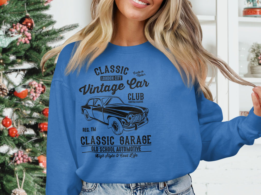 Indoors, someone sports a blue vintage car sweatshirt by Garment Graphics with text about a classic car club. Behind them, a decorated Christmas tree enhances the festive ambiance, perfectly aligning with Classic London Citys automotive style.
