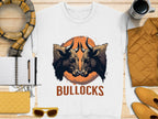 The striking white sweatshirt by Garment Graphics features a bullocks graphic with two bulls against a sunset and BULLOCKS below. Pair it with a yellow quilted jacket, notebook, pen, coffee cup, scarf, glasses, and clutch for a perfect laid-back style.