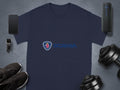 A navy blue cotton t-shirt by Garment Graphics features the Scania logo, flanked by a smartphone, smartwatch, portable speaker, dumbbells, and black sneakers on a gray surface—a must-have for Scania merchandise fans.