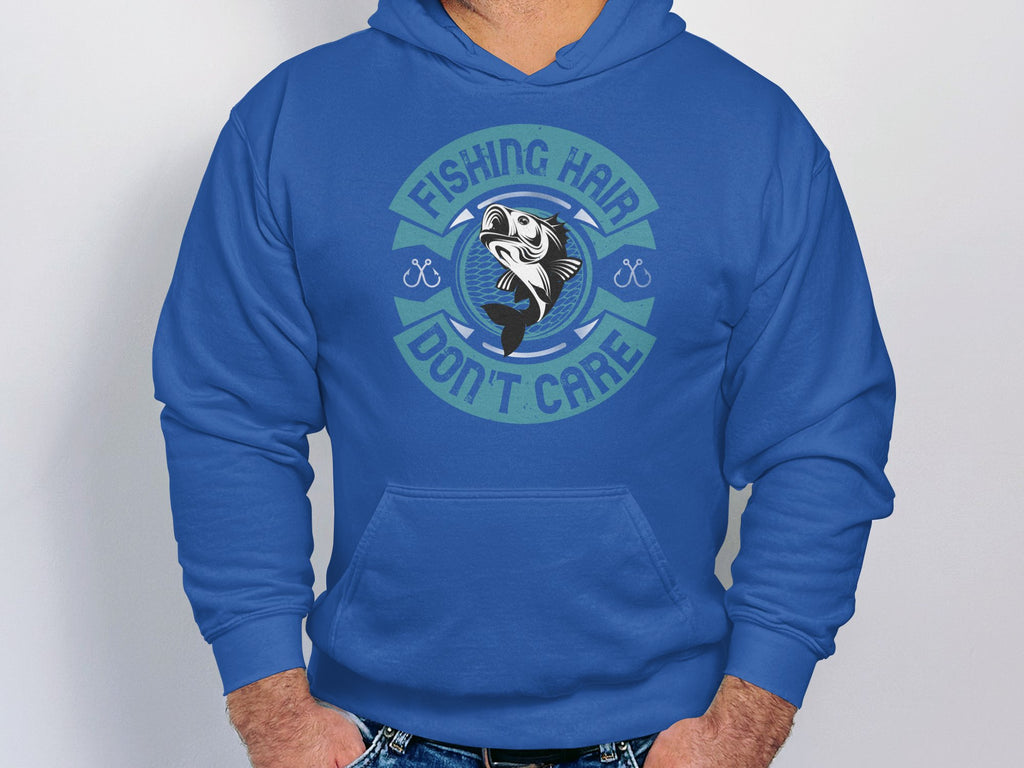 A person wears a Garment Graphics hoodie featuring the text Fishing Hair Dont Care around a fish image. Standing with hands in jeans pockets, they look poised for an angling adventure, with the focus on their torso.