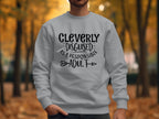 Amidst autumn foliage in a park, someone wears a light gray Garment Graphics sweatshirt with black lettering that humorously states, Cleverly disguised as a responsible adult. Part of the unisex Responsible Adult Sweatshirts collection, it combines style and wit effortlessly.