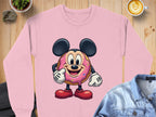 A playful pink sweatshirt by Garment Graphics features a cartoon donut with a character wearing mouse ears and gloves. Displayed on wood with a denim jacket, cactus, latte, and cloth item, it makes a fun wardrobe addition.