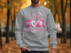 Someone is wearing a Garment Graphics gray sweatshirt featuring an illustrated pink and gray headphone design. The Just be cool Rock and Roll text stands out in pink and white, set against autumn trees, creating a trendy piece for music enthusiasts.