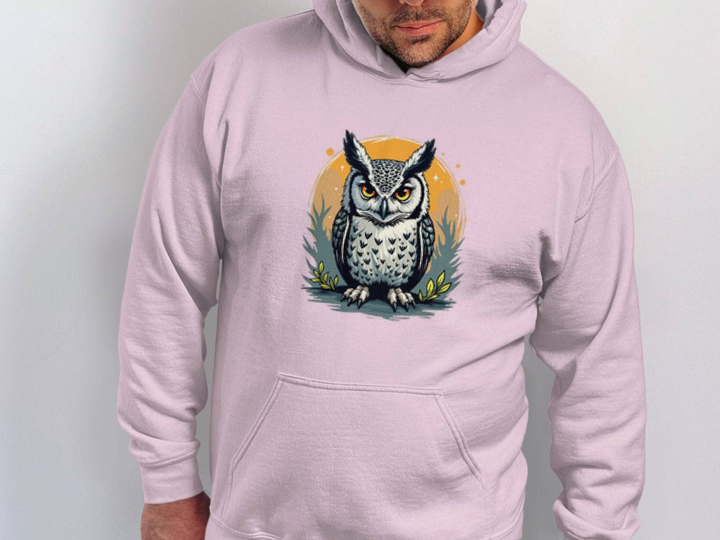 A person wears a Garment Graphics medium-heavy hoodie featuring a striking owl design on the front, set against a circular foliage backdrop. The classic fit hoodie allows them to face forward with hands in the pockets.