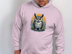 A person wears a Garment Graphics medium-heavy hoodie featuring a striking owl design on the front, set against a circular foliage backdrop. The classic fit hoodie allows them to face forward with hands in the pockets.