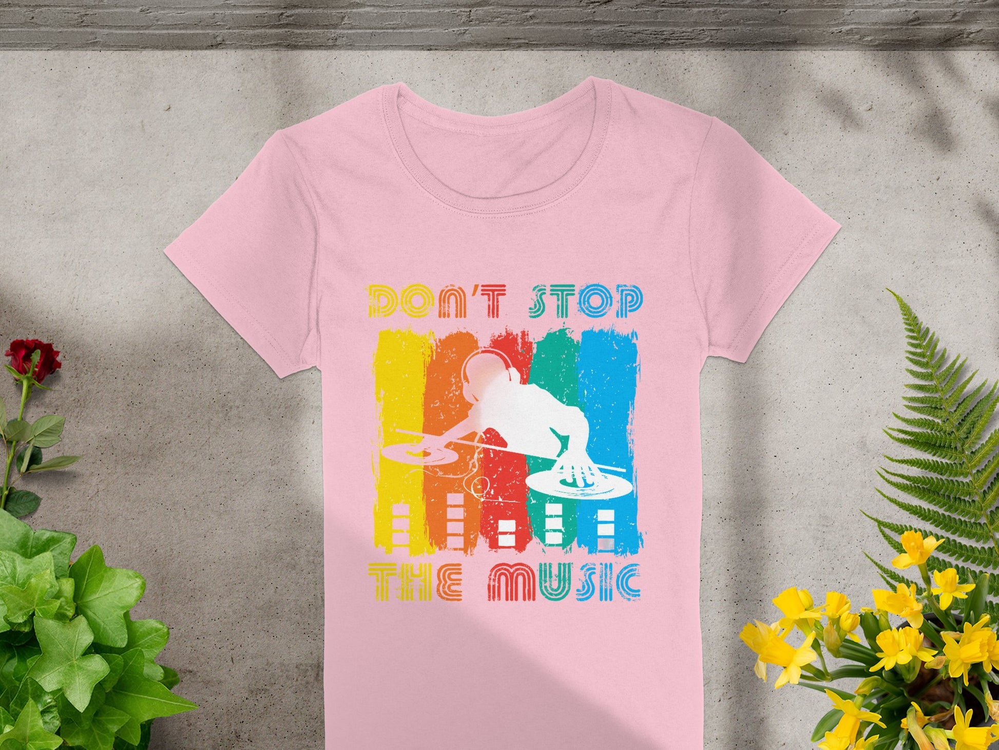 Garment Graphics presents a pink DJ graphic tee with turntables and Dont Stop the Music text. The dynamic background features blue, red, orange, and yellow stripes, with flowers on a concrete design—a must-have for music lovers.