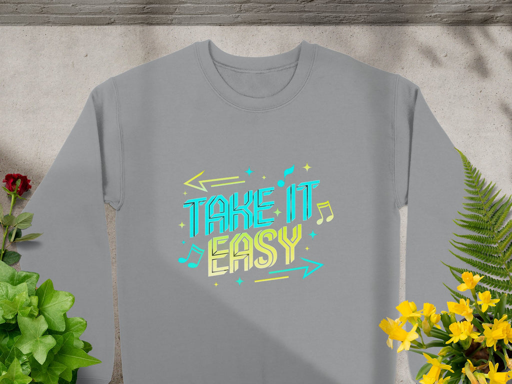 Garment Graphics presents a unisex sweatshirt, showcasing the Take It Easy design in blue and yellow with arrow and music note accents. Set among greenery on concrete, its ideal for casual wear.