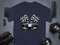 A Garment Graphics navy blue T-shirt displays a Formula One car and crossed checkered flags. The shirt is styled with a smartphone, smartwatch, speaker, sneakers, and dumbbells on a sleek gray background.