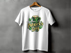 A white Happy Patricks Day T-Shirt by Garment Graphics hangs on a gray backdrop, featuring green text, a frothy beer mug, and scattered shamrocks. This lively shirt is ideal for celebrations, making it a fun way to embrace the festive spirit.
