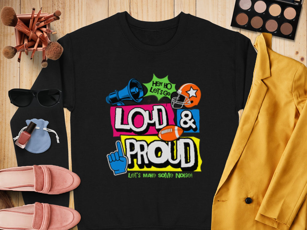 Garment Graphics presents a unique black unisex shirt with vibrant text, Hey Ho Lets Go Loud & Proud Lets Make Some Noise! accompanied by symbols like a megaphone, football helmet, and foam finger. Styled on wood with cosmetics, a yellow blazer, and pink shoes for added flair.