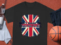 A classic fit black t-shirt from Garment Graphics, featuring DONT BLAME ME, I Didnt Vote For Him with a British flag design, lies on a textured orange surface. Surrounded by a water bottle, towel, shorts, and basketball, its the perfect outfit for expressing your opinion.