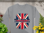 A gray Garment Graphics sweatshirt with a Union Jack and Dont Blame Me, I Didnt Vote For Him lies flat among green and yellow potted plants on a textured surface. This unisex piece adds a bold statement to any wardrobe.