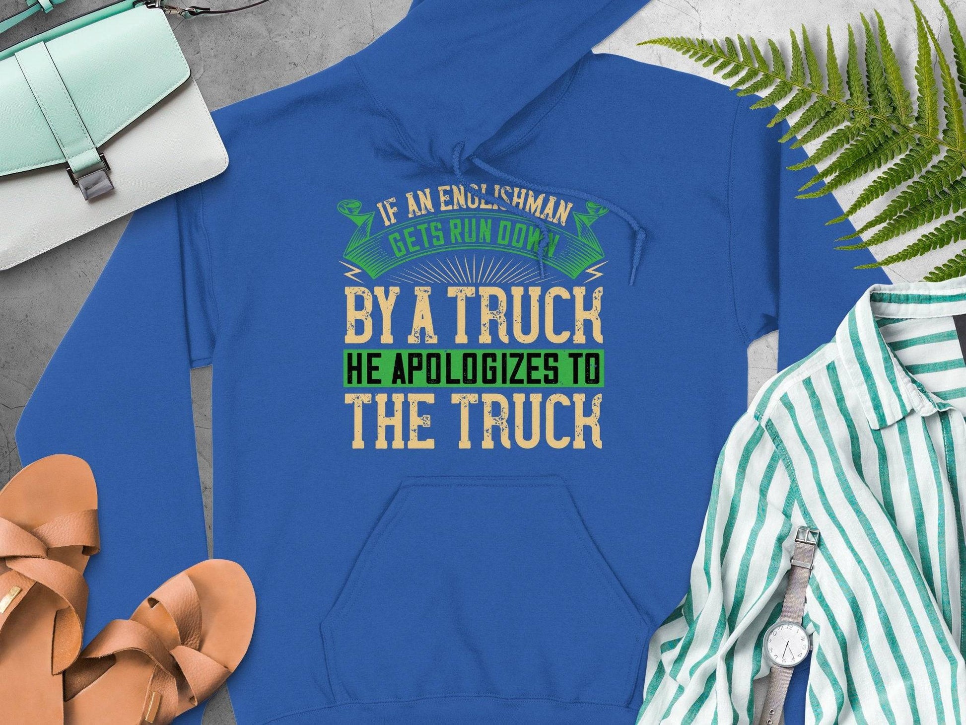 Garment Graphics presents a humorous hoodie with the quote: If an Englishman gets run over by a truck, he apologizes to the truck. Styled with sandals, a green-and-white striped shirt, purse, and fern leaves—an amusing nod to English etiquette.