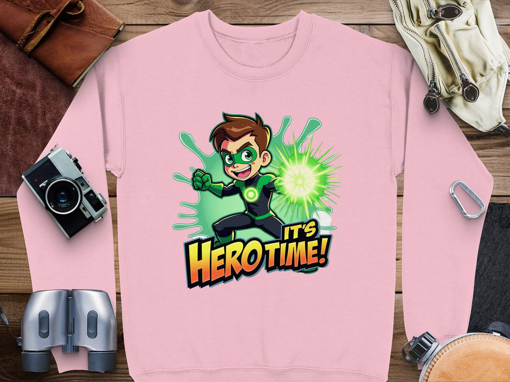 The pink graphic print sweatshirt from Garment Graphics showcases a brown-haired superhero in a green costume emitting green energy. The bold phrase Its Hero Time! is featured, and the unisex sizing guarantees a perfect fit. Accompanying items include a camera, binoculars, compass, and leather accessories.