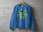 The Garment Graphics blue shamrock graphic sweatshirt features Happy St. Patricks Day in green and gold letters, surrounded by green shamrocks and a top hat, exuding festivity against a gray wall.