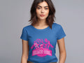 A woman with shoulder-length brown hair is wearing a blue Garment Graphics T-shirt featuring a pink Always Party Beach Girl graphic, set against a gray background.