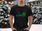 In a snowy landscape, someone wears a Garment Graphics black t-shirt boasting Irish pride with a green pickup truck and shamrocks, reading Happy St. Patricks Day in black text, framed by serene trees and snow.