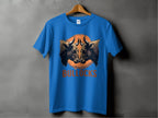 A blue T-shirt from Garment Graphics Bullocks Pintable line features a bulls face graphic and BULLOCKS text, hanging against an orange background. Available in Family Sizing for a cohesive look, it offers a Classic Fit.