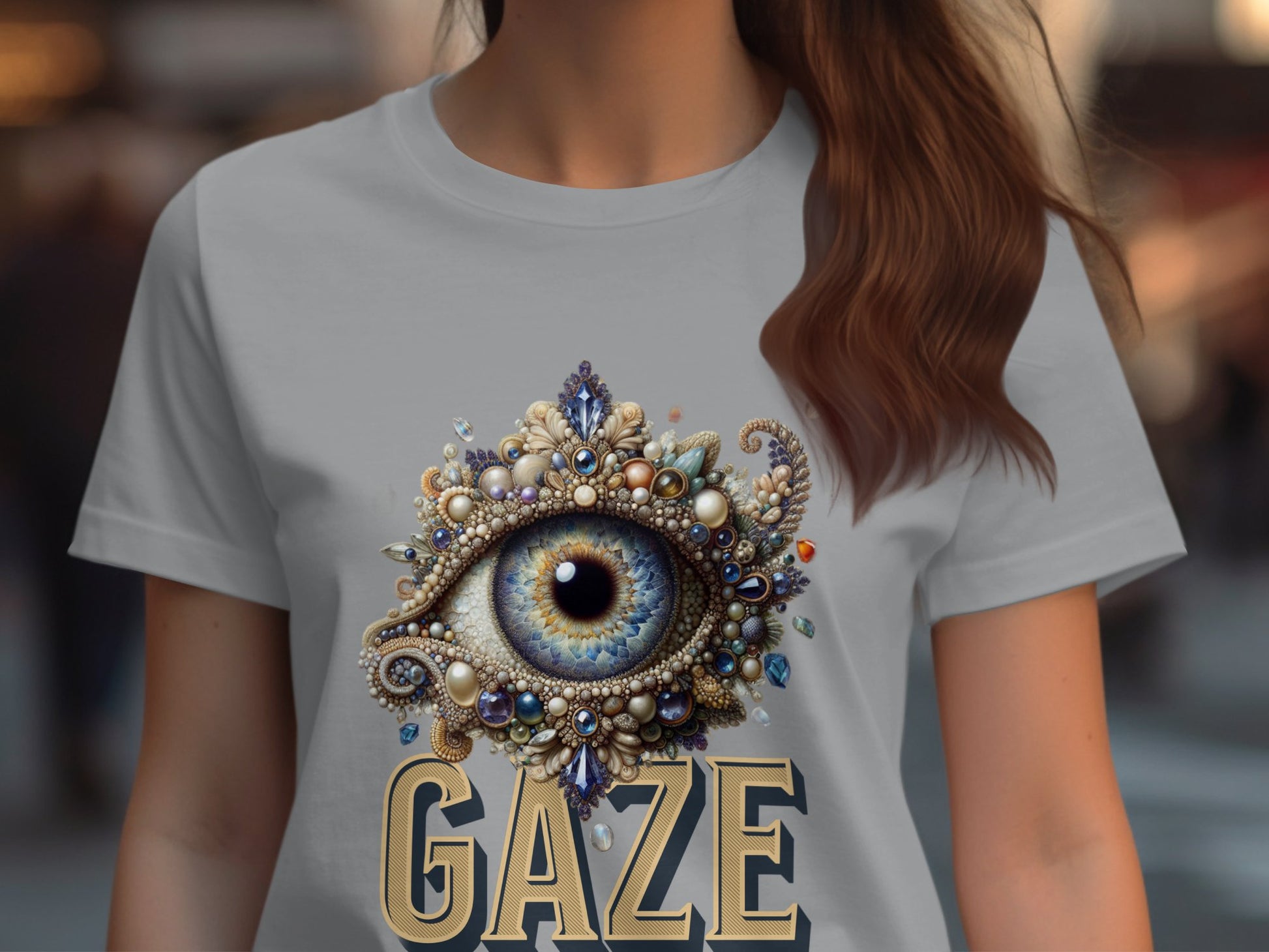 A woman in a Garment Graphics T-shirt displays an ornate eye crafted from jewels and pearls, with GAZE boldly below. The intricate details and soft-focus backdrop highlight the shirts allure.
