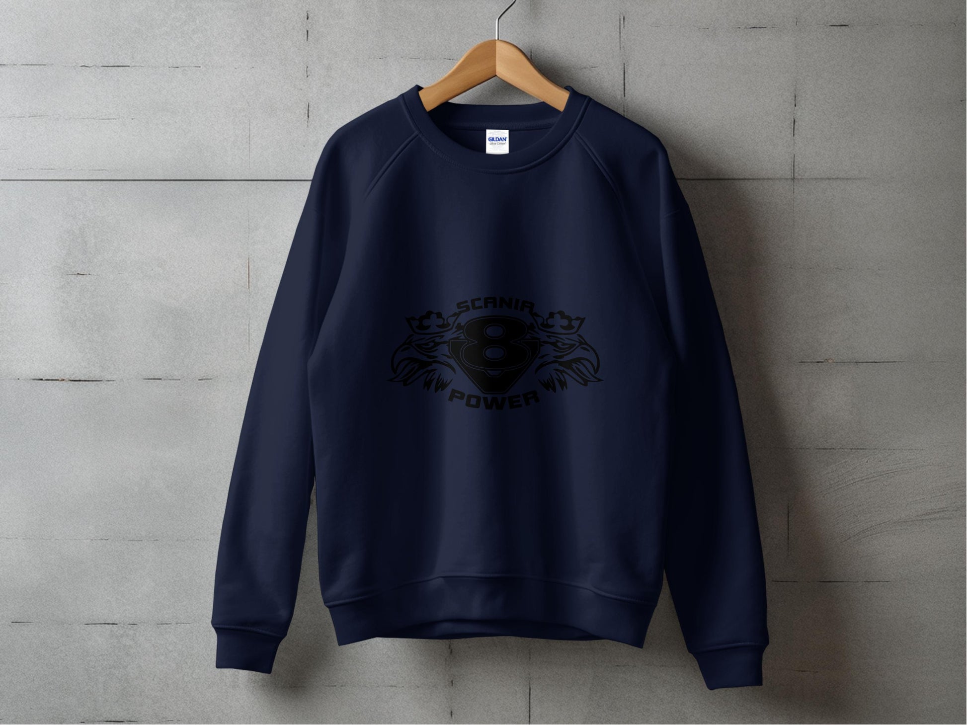 A navy blue sweatshirt from Garment Graphics hangs against a gray concrete wall, displaying the bold Scania Power 8 logo at its center, surrounded by stylized graphics. With a crew neck and long sleeves, it combines comfort and style.