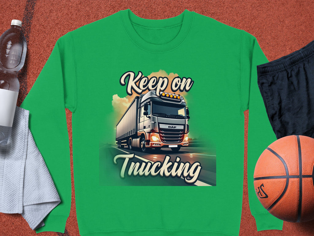 A green graphic sweatshirt from Garment Graphics, featuring a truck illustration and Keep on Trucking text, is displayed on an orange surface with a basketball, black shorts, a gray towel, and a water bottle.
