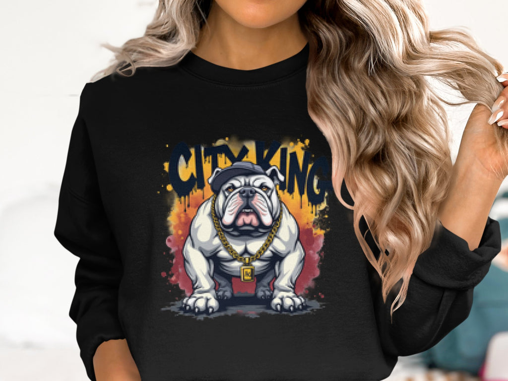 A person with long, wavy blonde hair is rocking a trendy Garment Graphics Bulldog Sweatshirt. The black sweatshirt features a stylish bulldog illustration adorned with gold chains and a baseball cap, along with the bold phrase City King above it.