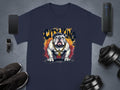 A navy blue Garment Graphics T-Shirt features an angry bulldog design with sunglasses and a gold chain, topped by the words CITY KING. Laid on a gray surface, its surrounded by essentials like a phone, smartwatch, speaker, sneakers, and dumbbells.