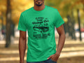A man in a Garment Graphics green T-shirt with Vintage Car Club design stands against a blurred outdoor autumn backdrop.