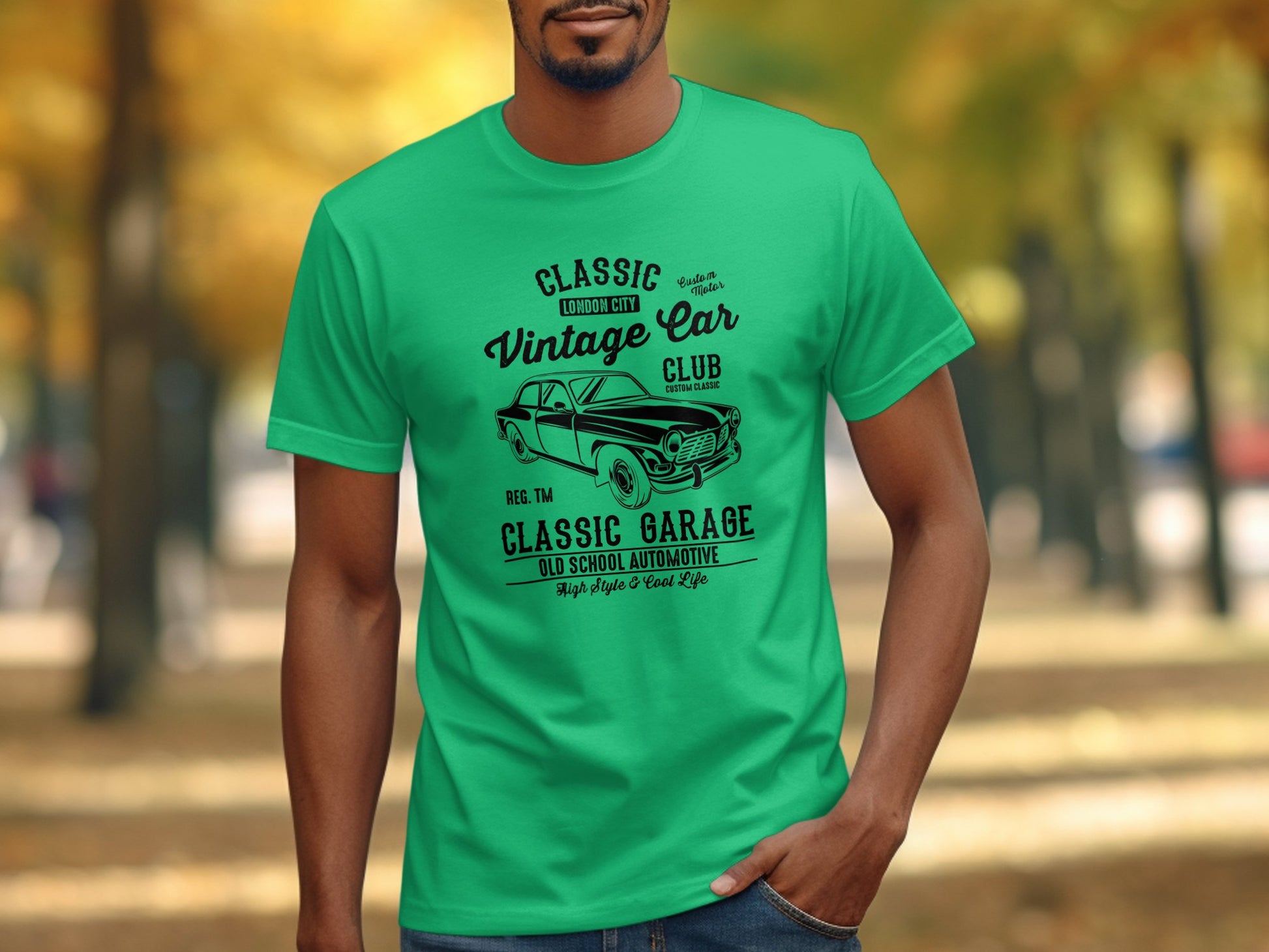 A man in a Garment Graphics green T-shirt with Vintage Car Club design stands against a blurred outdoor autumn backdrop.