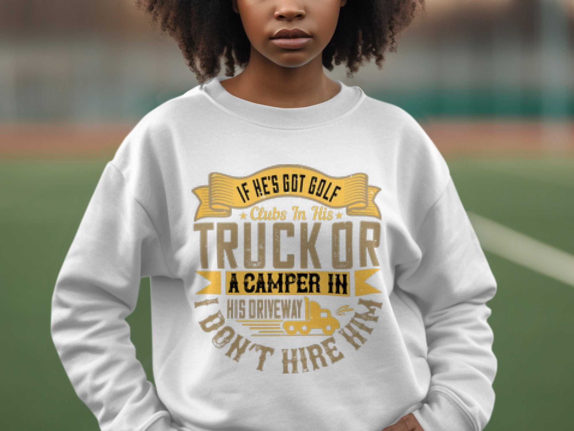 A woman showcases her unique style in a Garment Graphics white sweatshirt with the witty phrase, If hes got golf clubs in his truck or a camper in his driveway, I dont hire him, standing outdoors against a blurred backdrop.