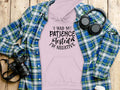 A light pink Garment Graphics hoodie featuring the humor-filled quote, I had my patience tested, Im negative, is styled on a wooden surface with a blue plaid shirt, headphones, and a camera—ideal for highlighting its unique design and flair.