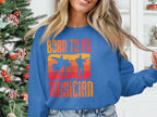Inside, a person dons Garment Graphics blue unisex sweatshirt featuring Born to Be Musician and silhouettes of musicians. A festive Christmas tree decor enhances the atmosphere, making it an ideal pick for music enthusiasts.