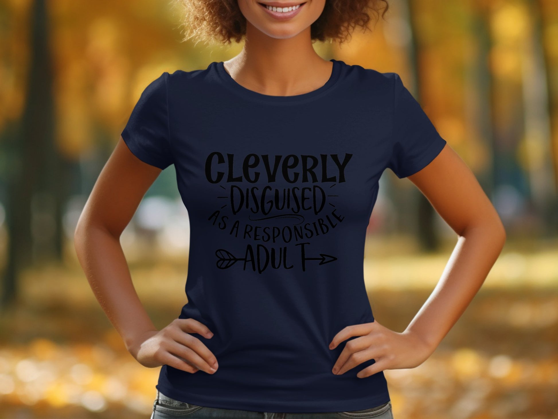 In a park with autumn leaves, someone stands confidently wearing Garment Graphics semi-fitted navy blue T-shirt. The shirt humorously displays Cleverly Disguised as a Responsible Adult in bold black text, featuring playful arrow graphics.