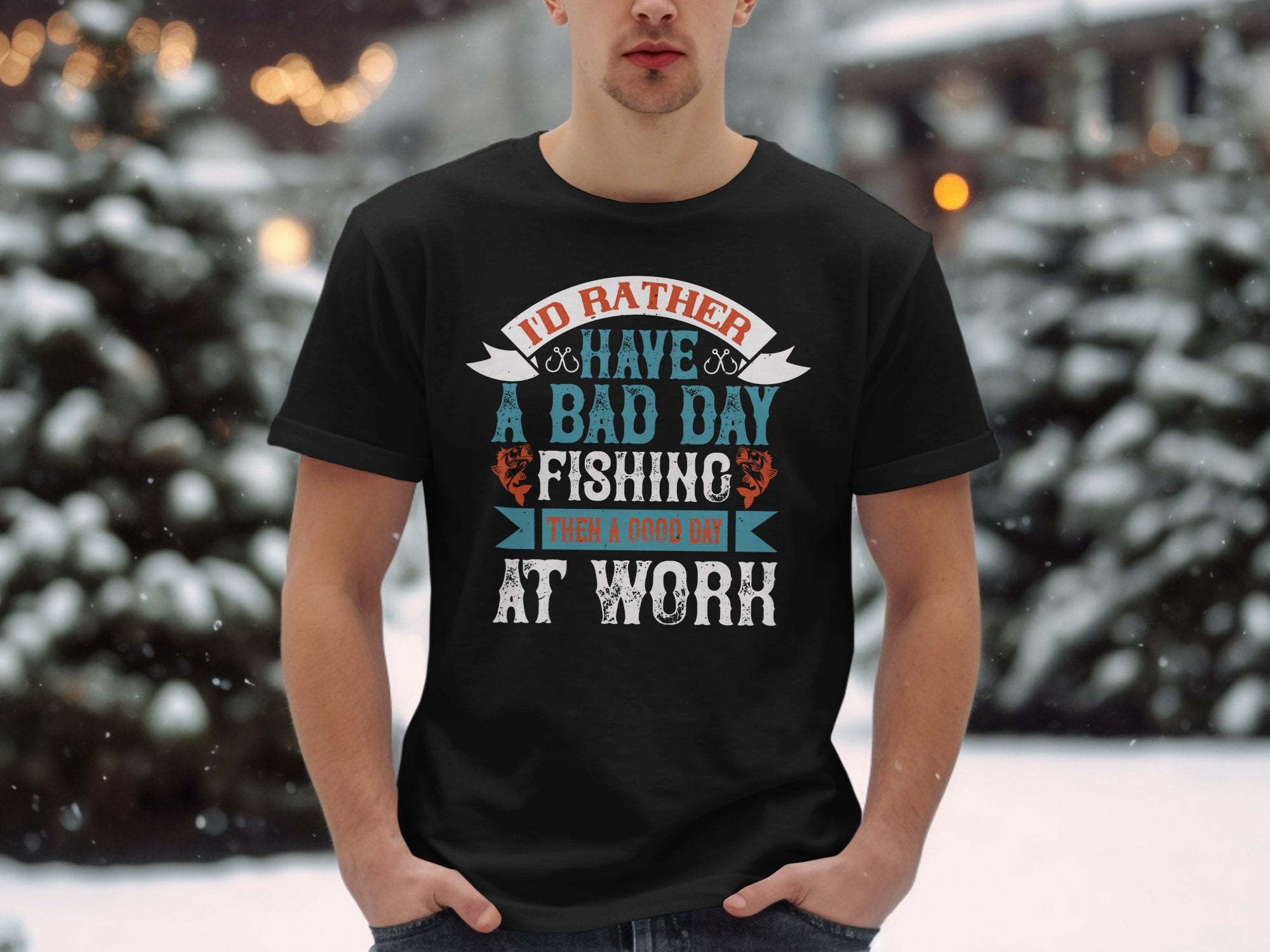 A person stands in the snow, proudly wearing a Garment Graphics black fishing T-shirt featuring colorful text: Id rather have a bad day fishing than a good day at work. It’s an ideal gift for passionate anglers.
