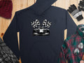 The Garment Graphics navy blue hoodie, ideal for motorsport fans, features a race car and checkered flags. Its displayed on a wooden surface with chic accessories: a knit hat, gloves, plaid shirt, and scarf.