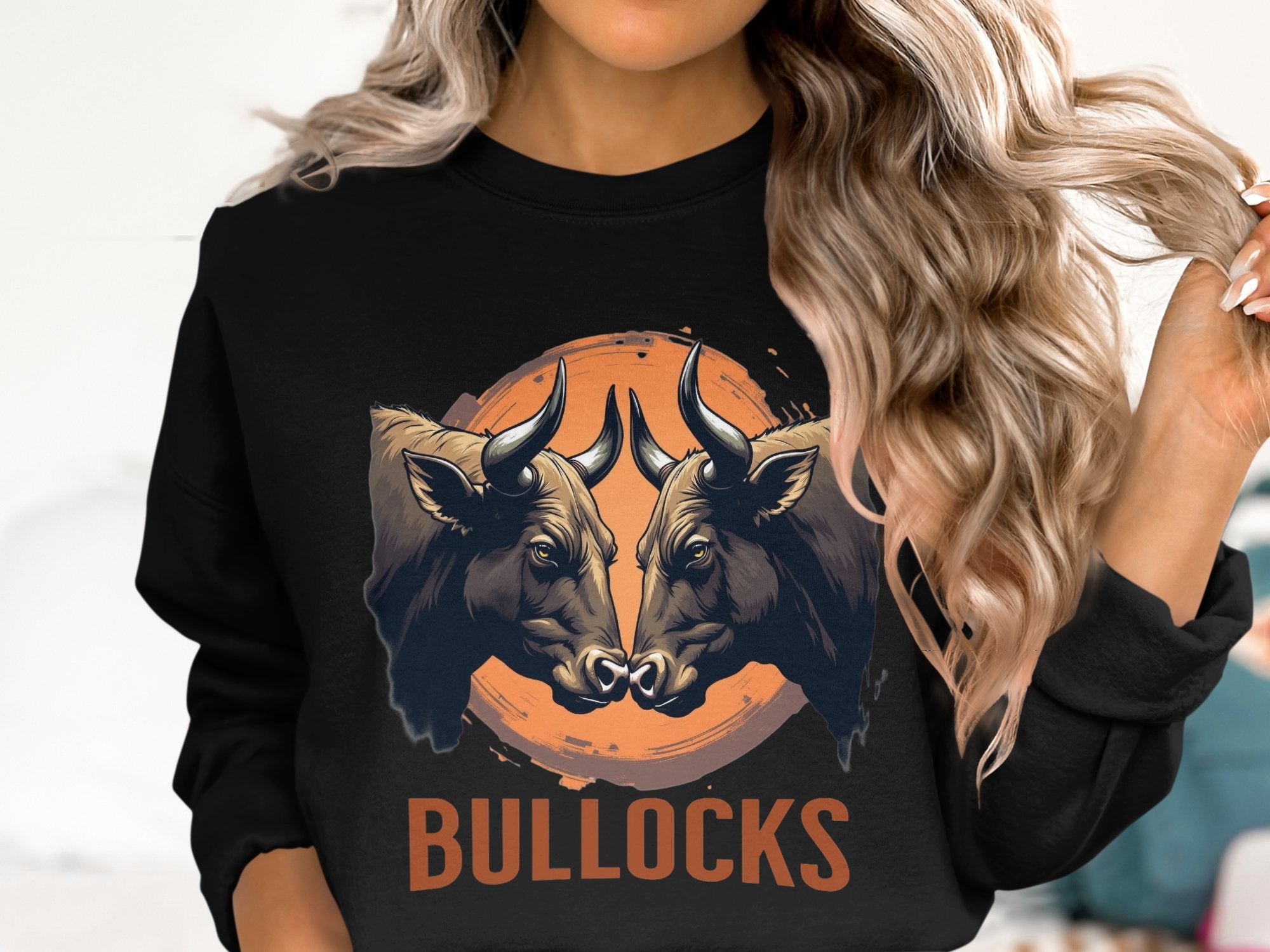 A person with long wavy hair is sporting an eye-catching loose-fit black sweatshirt by Garment Graphics, featuring a striking print of two bulls with large horns facing each other and BULLOCKS boldly printed underneath, adding flair to the design.