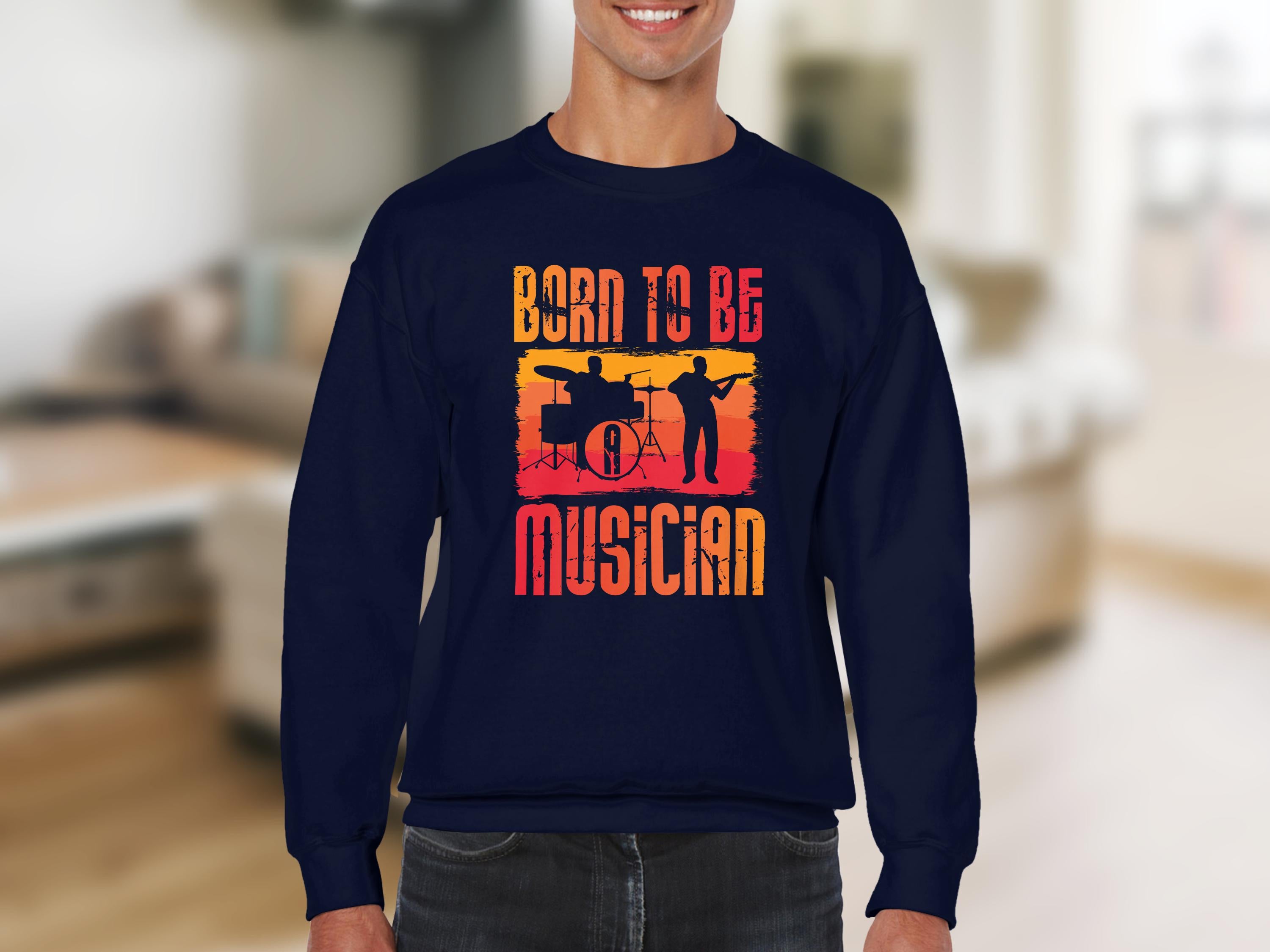 Indoors, a person wears a Garment Graphics dark sweater with Born to Be Musician, featuring drummer and guitarist silhouettes on a vivid red and yellow backdrop. This unisex design is ideal for music lovers. The room background is softly blurred.