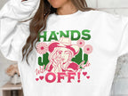 A person wears a Garment Graphics loose-fit white sweatshirt with a cartoon cowgirl holding a gun, text HANDS OFF! Wild Side, embellished with flowers and hearts, making it a standout Hands Off Wild Side Sweatshirt.