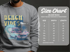 A person is wearing a Garment Graphics gray graphic sweatshirt with a vintage car, surfboards, palm trees, and Beach Vibes, ideal for a retro roadtrip. The Gildan 18000 size chart on the right shows unisex sizing from S to 5XL with measurements in inches.