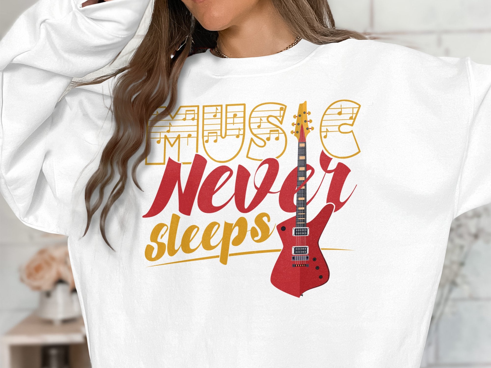 A music enthusiast wears a Garment Graphics sweatshirt with Music Never Sleeps in artistic fonts and a vibrant red electric guitar design, adjusting their long brown hair to embody the Music Never Sleeps Guitar spirit.