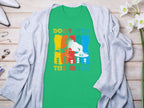 Garment Graphics offers a green t-shirt featuring a white DJ turntable graphic and the text Dont Stop the Music in vibrant letters. Displayed on wood with a gray cardigan, jewelry, and white flowers, its ideal for music-loving party-goers.