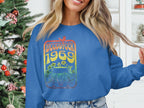 Someone in a blue Garment Graphics sweatshirt with a vintage 1969 Woodstock design stands next to a decorated Christmas tree. The retro rainbow palette, florals, and car perfectly capture the festivals spirit. The person has long hair and is partially cropped out of the frame.