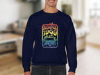 A person wearing a dark Garment Graphics sweatshirt exudes retro vibes with its vintage 1969 design, displaying the text Woodstock 1969 over a flower-adorned car and peace sign. A softly focused indoor living room in the background enhances the nostalgic atmosphere.