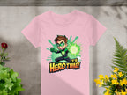 The Garment Graphics pink t-shirt showcases a young hero with a green superhero design and glowing fist, set against the phrase Its Hero Time! in bold. Lush plants surround this vibrant tee, laid out on a gray surface, making it perfect for adding color to any wardrobe.