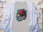 Paired with a light gray cardigan, the classic fit T-shirt showcases a fierce red bird graphic and bold Garment Graphics text on a wooden background. White flowers, jewelry, and white high-heeled shoes complete this elegant ensemble.