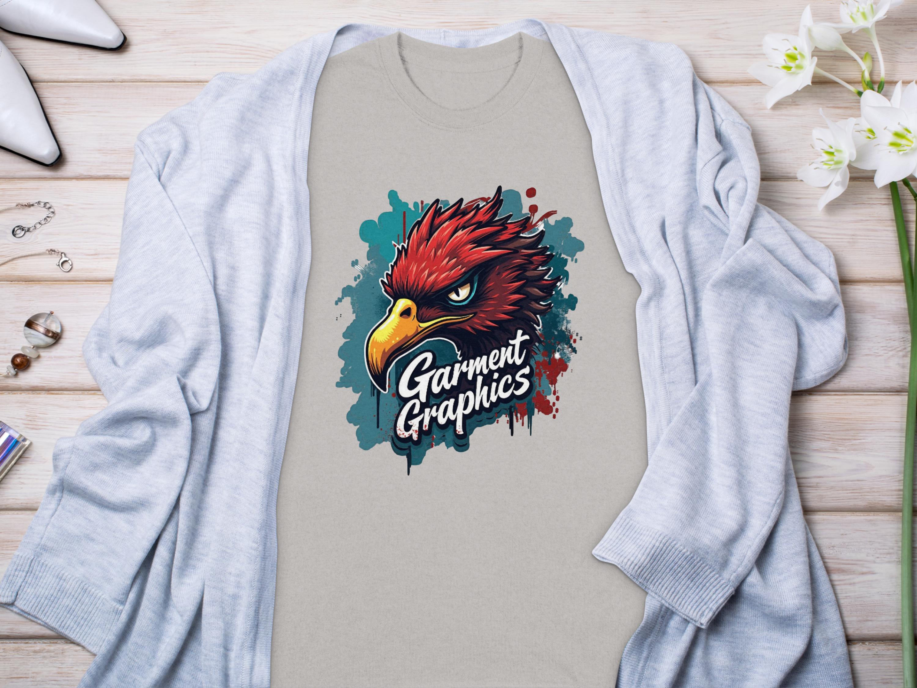 Paired with a light gray cardigan, the classic fit T-shirt showcases a fierce red bird graphic and bold Garment Graphics text on a wooden background. White flowers, jewelry, and white high-heeled shoes complete this elegant ensemble.
