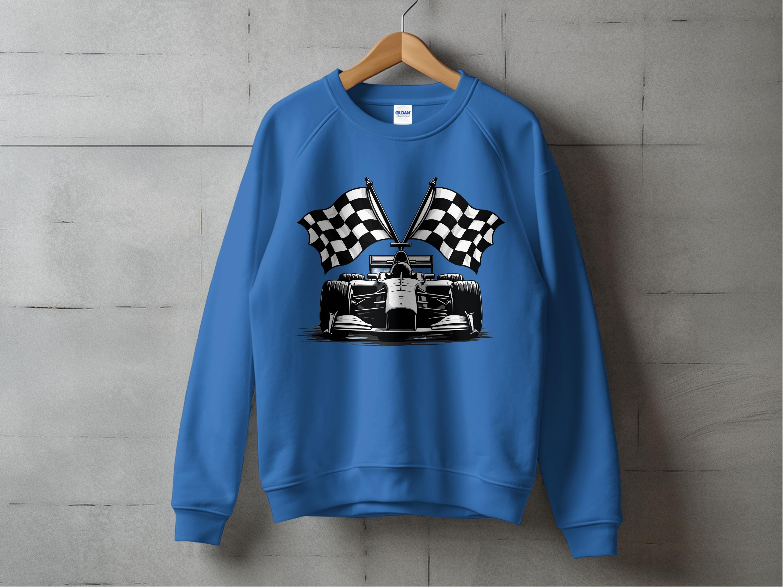 On a hanger against a concrete wall, the Garment Graphics blue racing car sweatshirt showcases a bold race car graphic with two crossed checkered flags, enhancing its distinctive checkered flag print appeal.