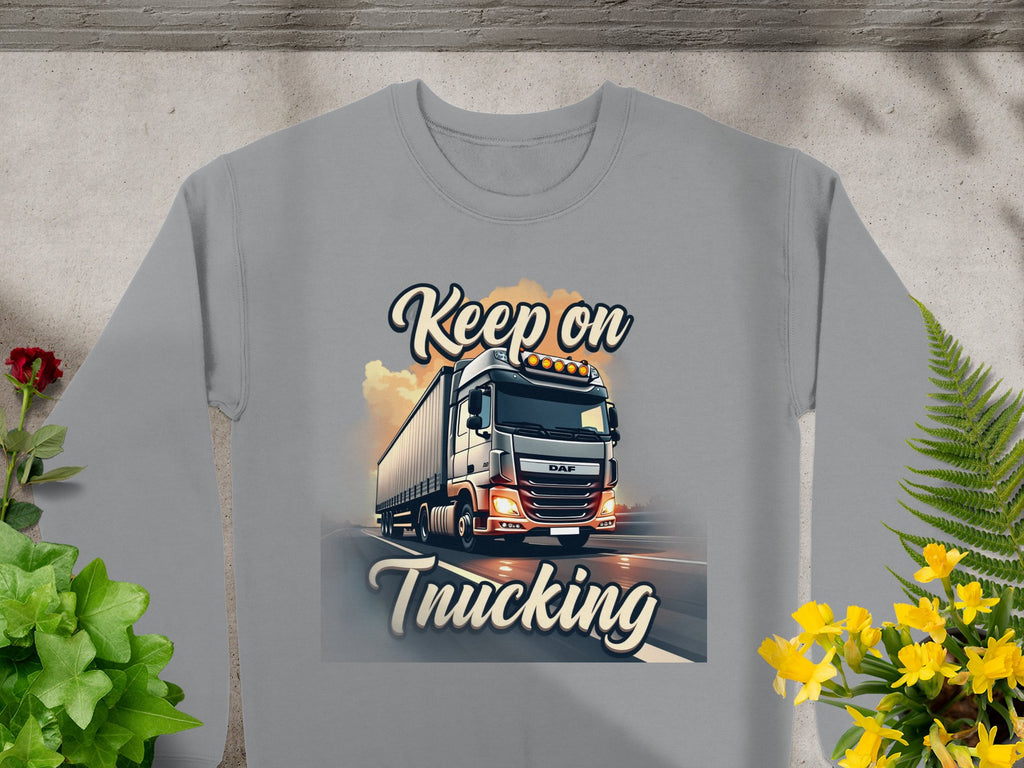 The Garment Graphics unisex gray graphic sweatshirt features a bold truck image on the road with Keep on Trucking text, surrounded by decorative plants—ideal for fans of lifes journeys.