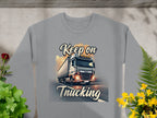 The Garment Graphics unisex gray graphic sweatshirt features a bold truck image on the road with Keep on Trucking text, surrounded by decorative plants—ideal for fans of lifes journeys.